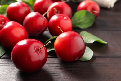 Photo of Delicious ripe cherry plums with leaves on wooden table, closeup