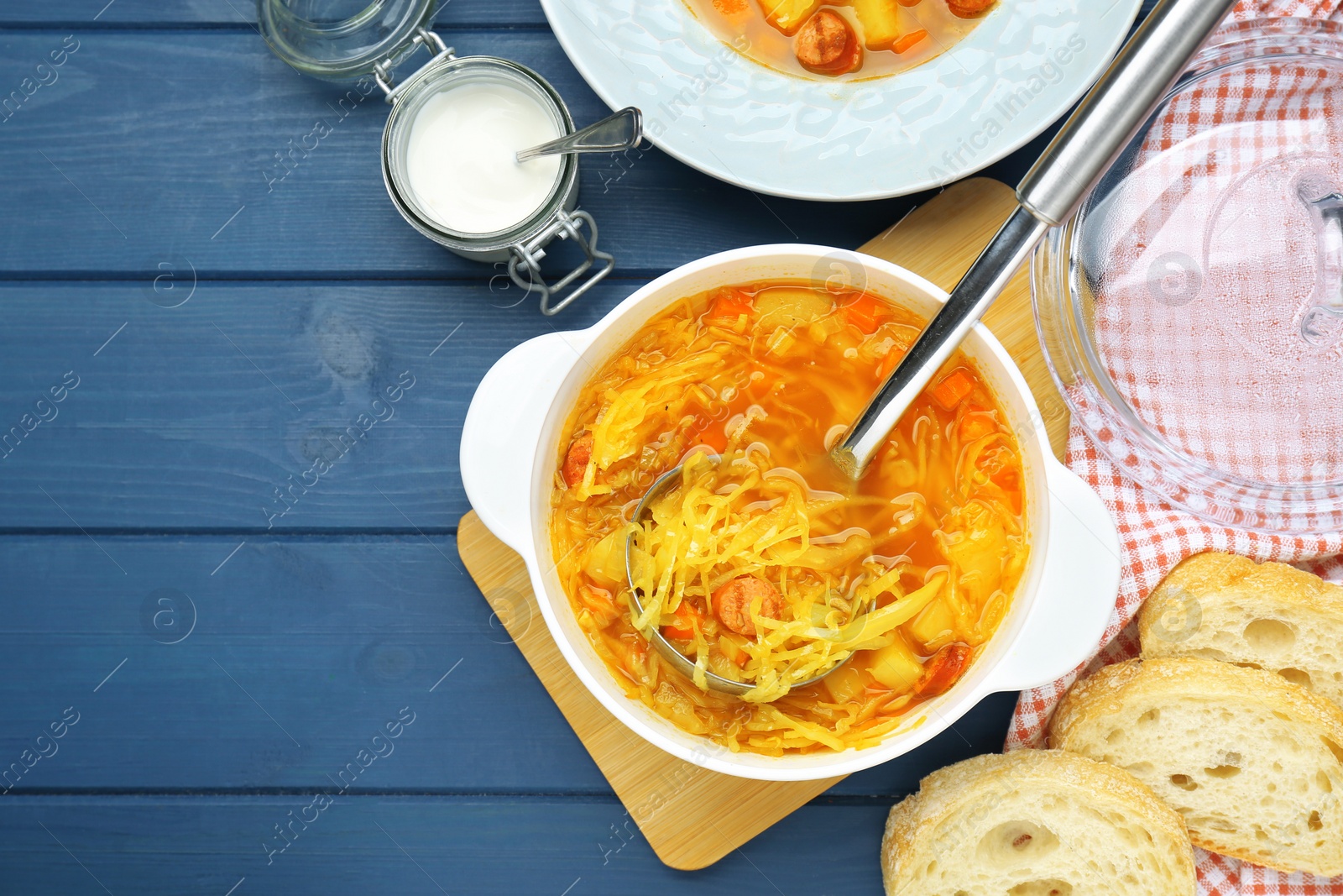 Photo of Delicious sauerkraut soup with smoked sausages served on blue wooden table, flat lay. Space for text