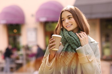 Photo of Beautiful woman in warm scarf with paper cup of coffee on city street, space for text