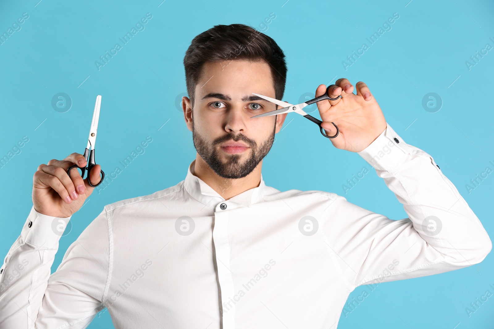 Photo of Young hairstylist holding professional scissors on color background