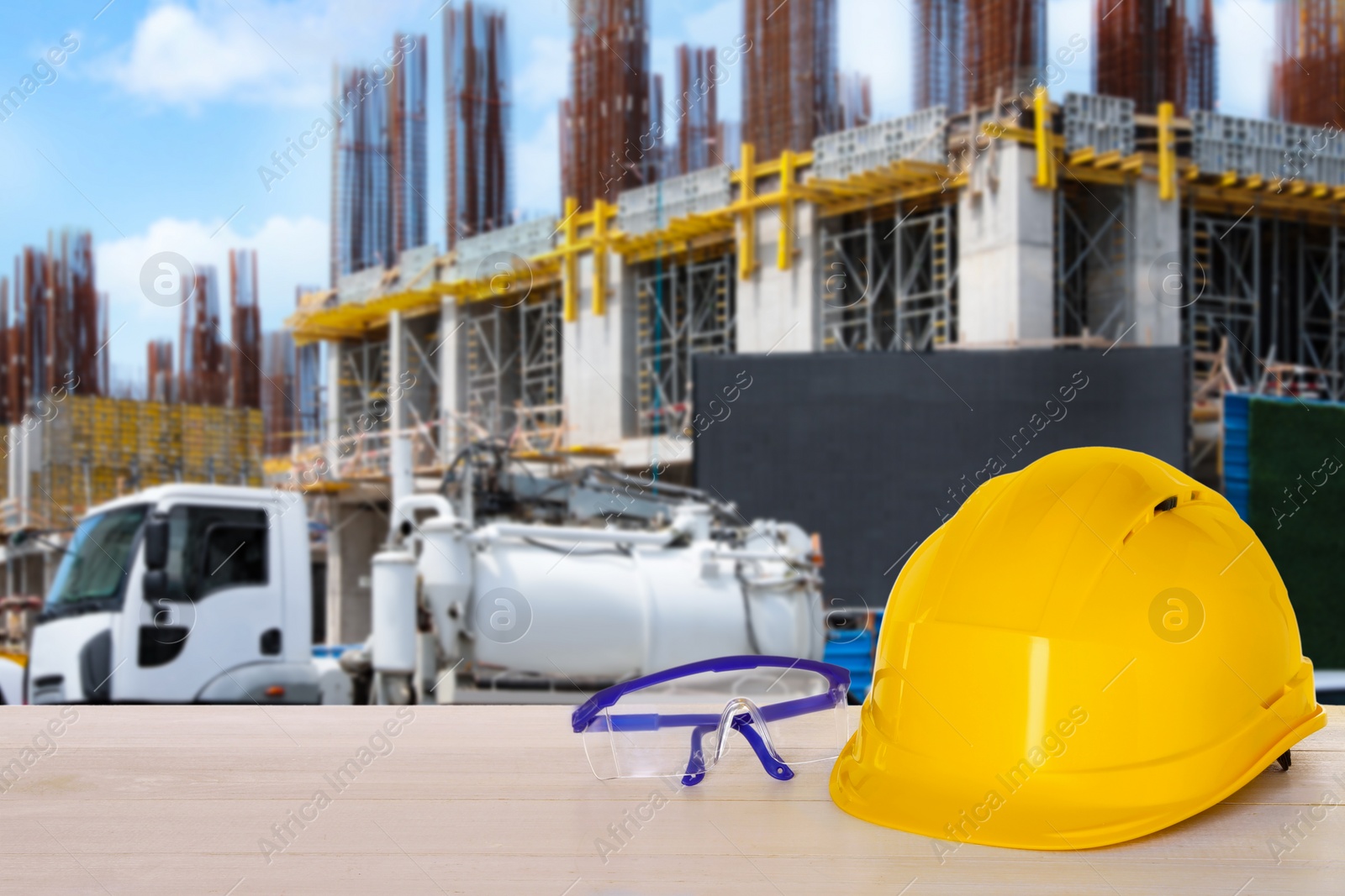 Image of Safety equipment. Hard hat and goggles on wooden surface near construction site and truck outdoors, space for text