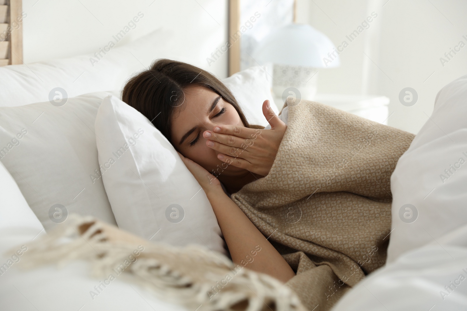 Photo of Woman covered with warm beige plaid lying in bed indoors