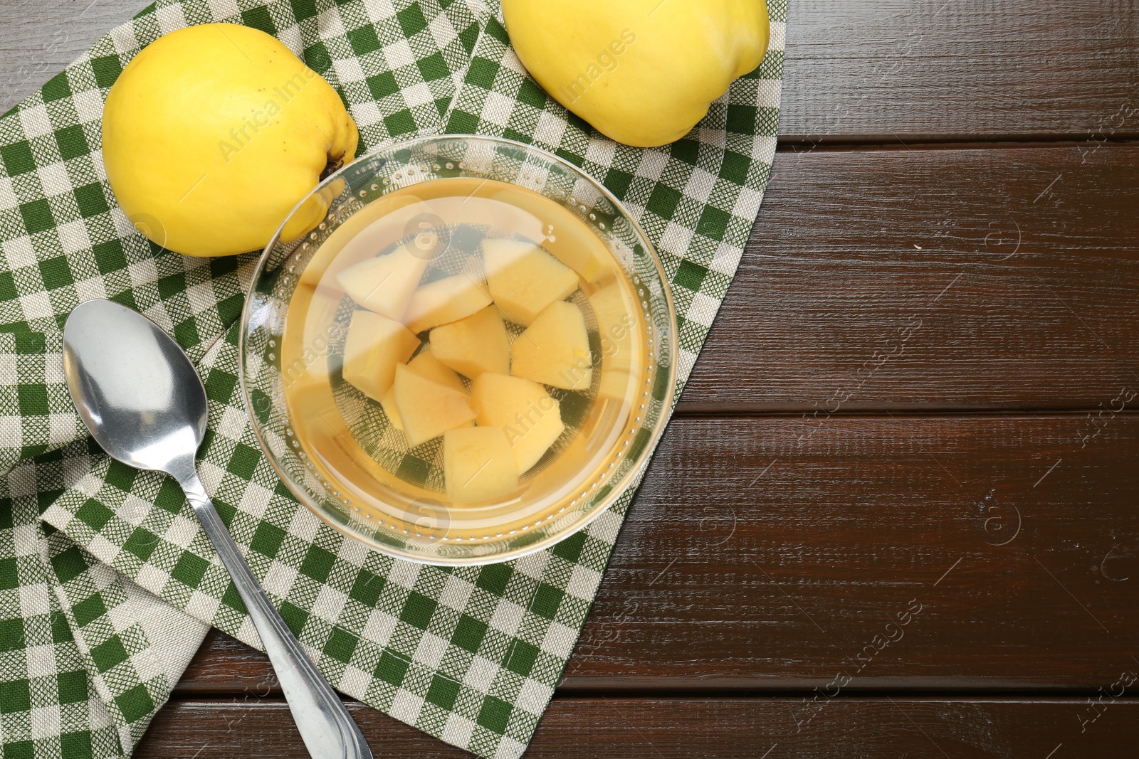 Photo of Delicious quince drink in glass bowl, fresh fruits and spoon on wooden table, top view. Space for text