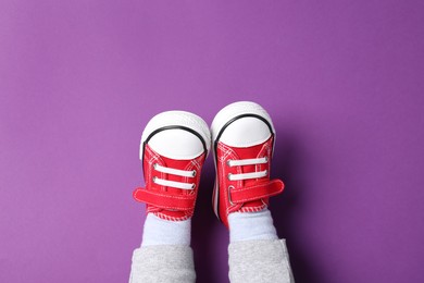 Photo of Little child in stylish red gumshoes on purple background, top view