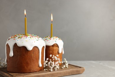 Photo of Tasty Easter cakes with burning candles on grey table. Space for text