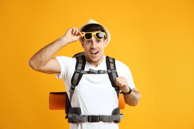 Photo of Emotional male tourist with travel backpack on yellow background
