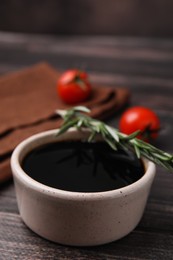 Photo of Bowl with balsamic vinegar, rosemary and tomatoes on wooden table, closeup