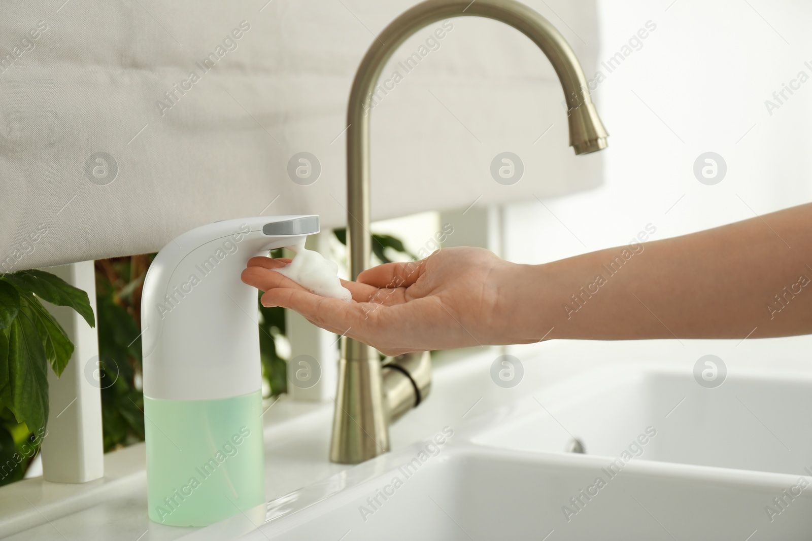 Photo of Woman using automatic soap dispenser in kitchen, closeup