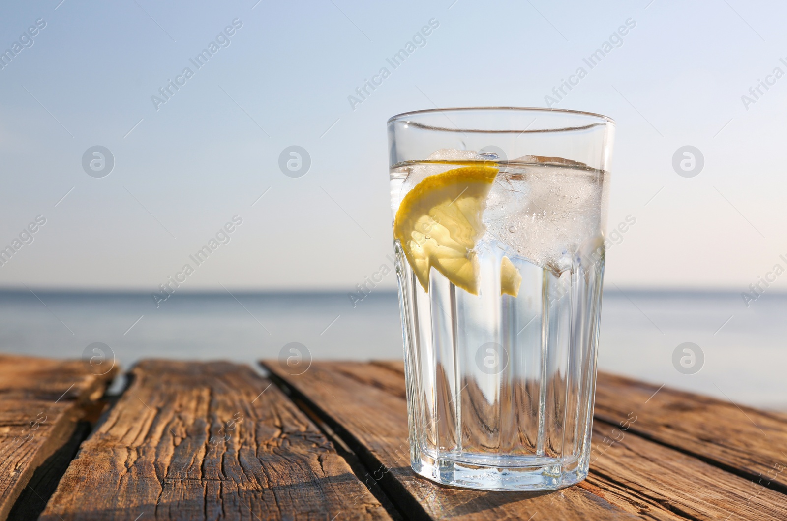 Photo of Wooden table with glass of refreshing lemon drink on hot summer day outdoors, space for text