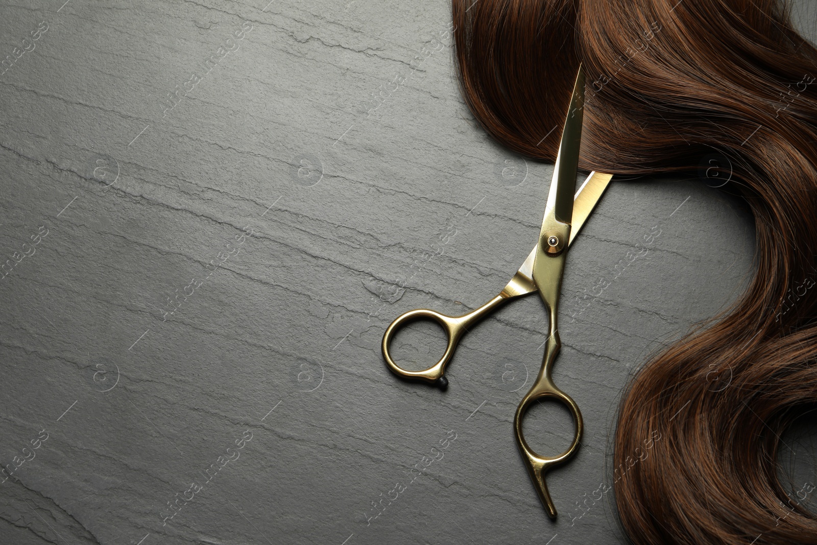 Photo of Professional hairdresser scissors with brown hair strand on dark grey table, top view. Space for text