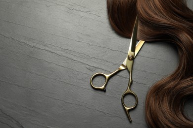 Professional hairdresser scissors with brown hair strand on dark grey table, top view. Space for text