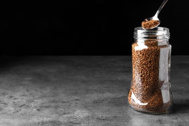 Photo of Instant coffee and spoon above glass jar on grey table against black background. Space for text