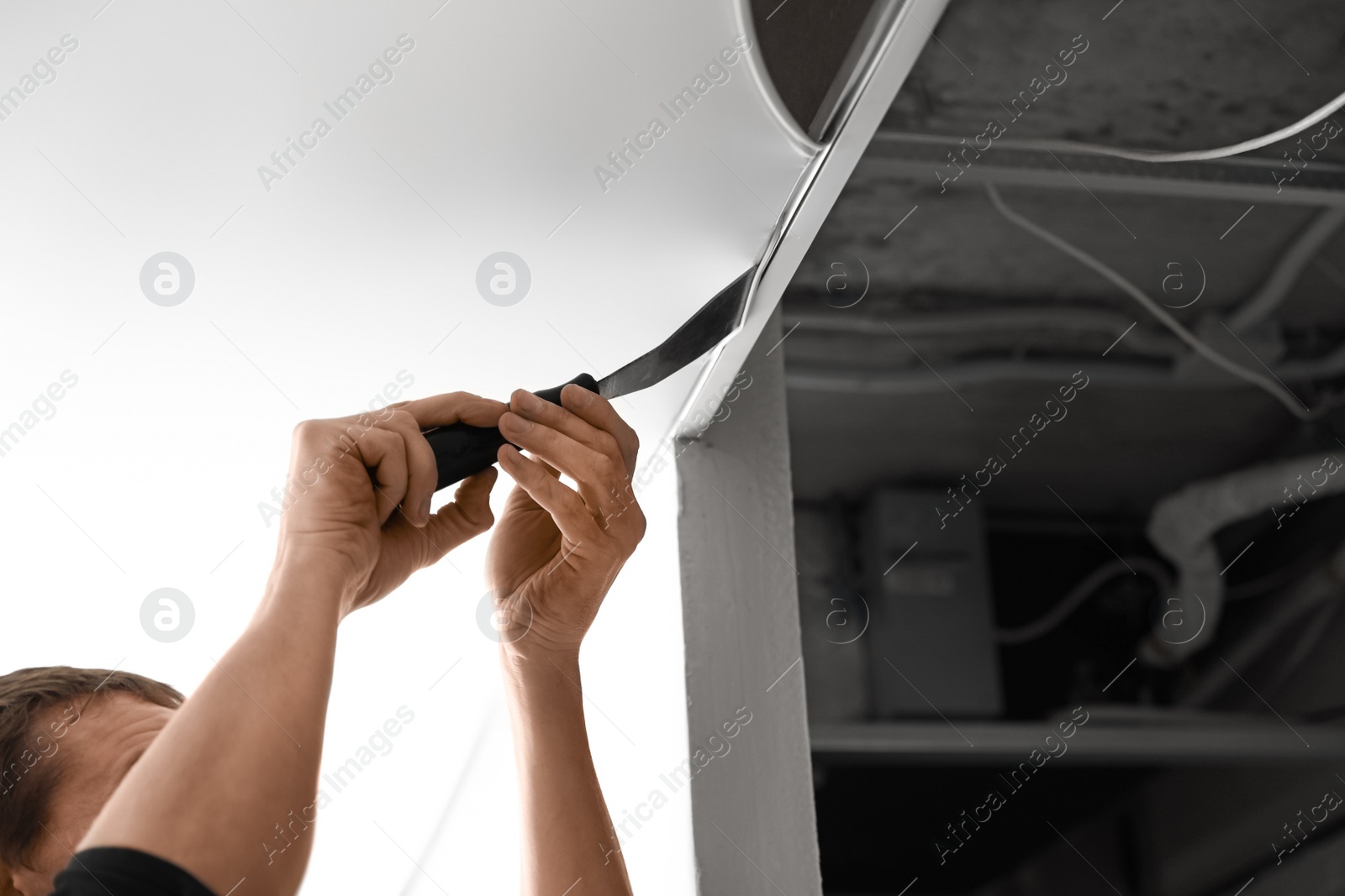 Photo of Repairman installing white stretch ceiling in room, closeup