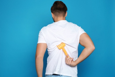 Young man scratching back with toy rake on color background. Annoying itch