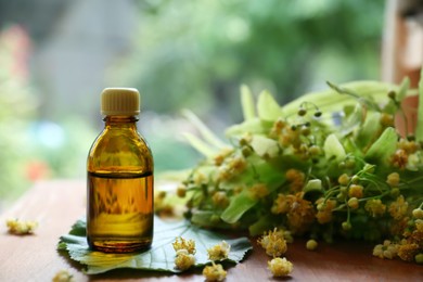 Bottle of essential oil and linden blossoms on wooden table against blurred background