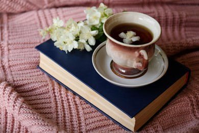 Photo of Cuparomatic tea with beautiful jasmine flowers and book on pink fabric