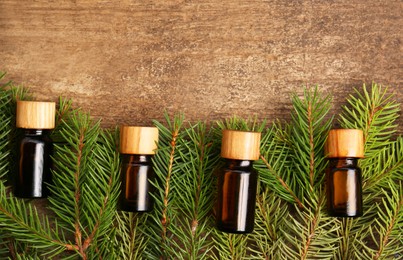 Photo of Bottles of pine essential oil and conifer tree branches on wooden table, flat lay. Space for text