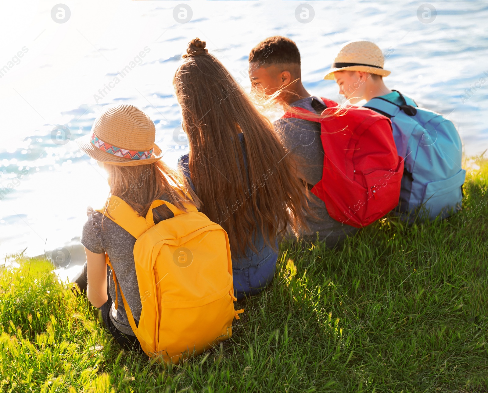 Image of School holidays. Group of children sitting on green grass near river 