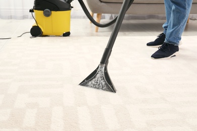 Photo of Man removing dirt from carpet with vacuum cleaner indoors, closeup