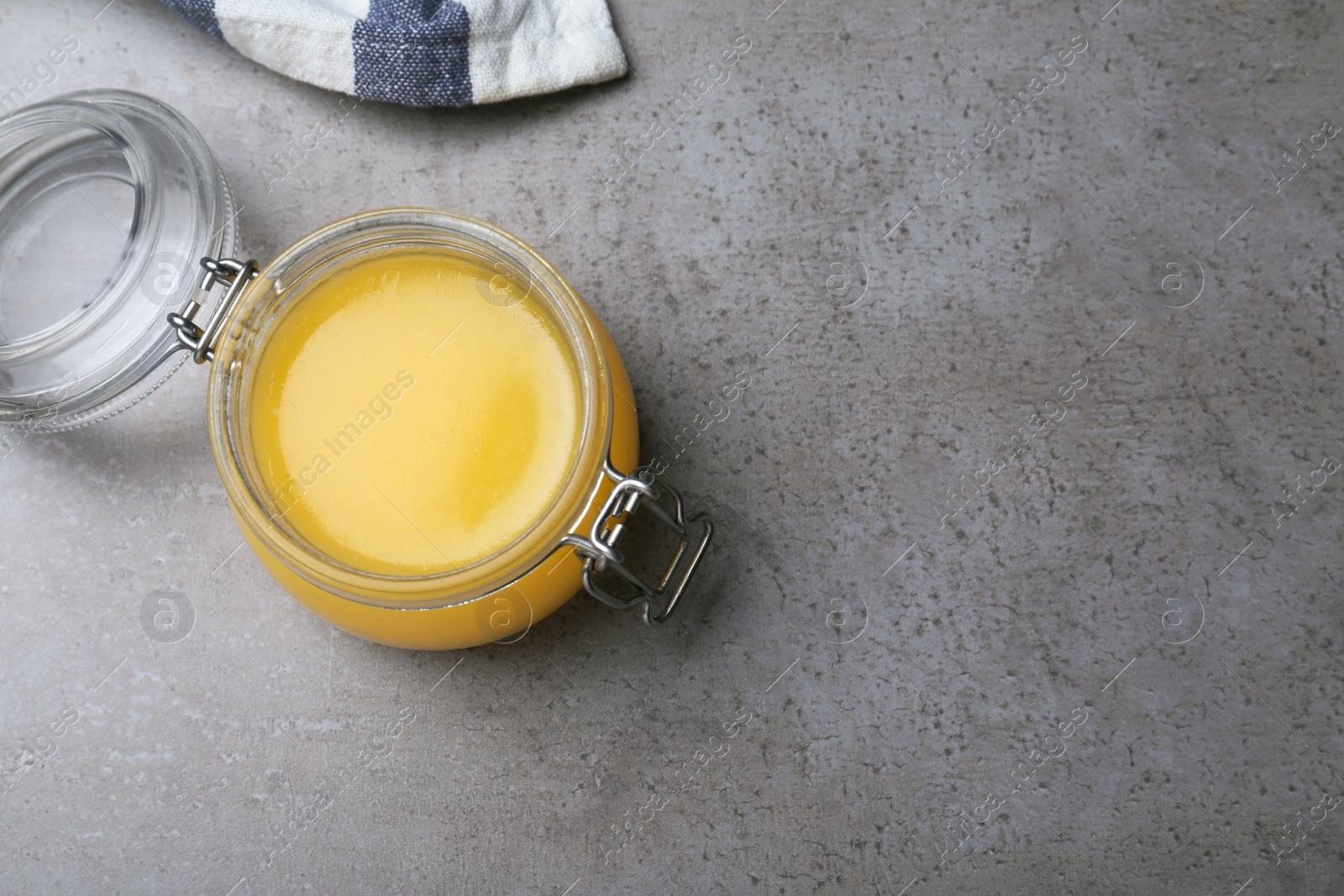 Photo of Glass jar of Ghee butter on grey table, top view. Space for text