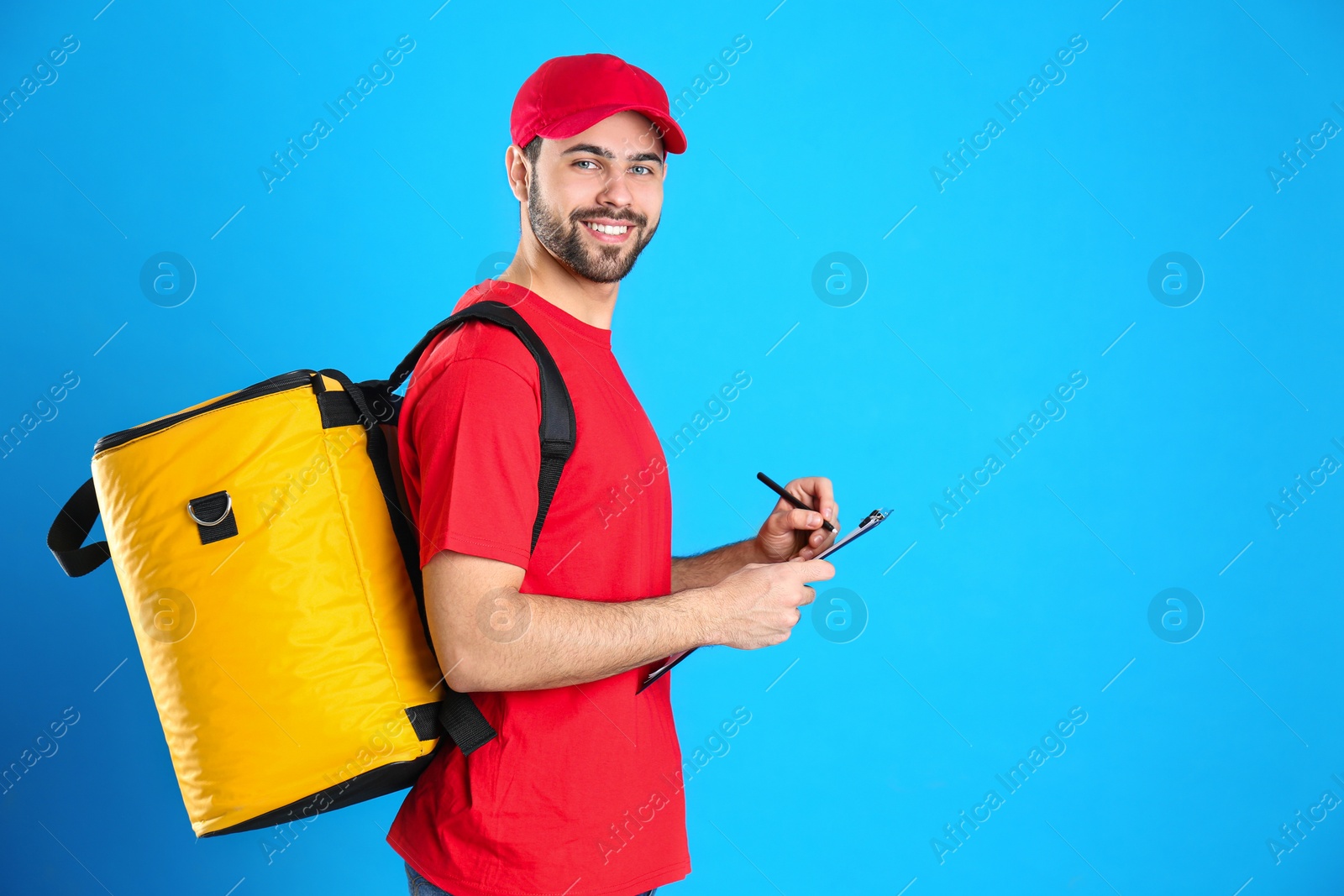 Photo of Courier with thermo bag and clipboard on light blue background, space for text. Food delivery service
