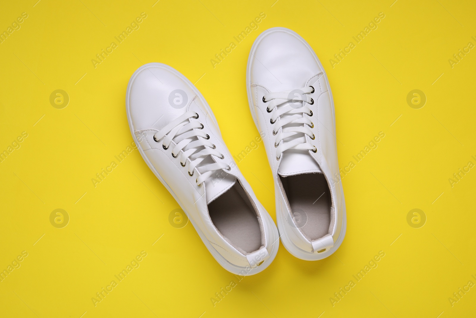 Photo of Pair of stylish white sneakers on yellow background, top view