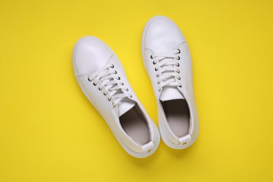 Pair of stylish white sneakers on yellow background, top view