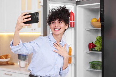 Photo of Smiling food blogger taking selfie near fridge in kitchen