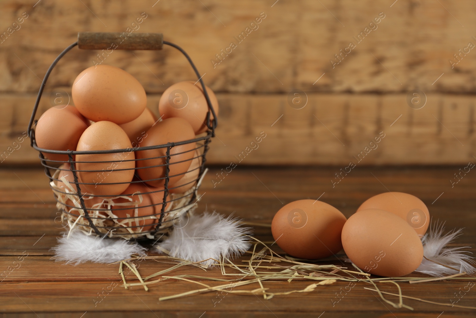 Photo of Raw chicken eggs, decorative straw and feathers on wooden table