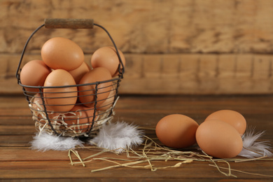 Photo of Raw chicken eggs, decorative straw and feathers on wooden table