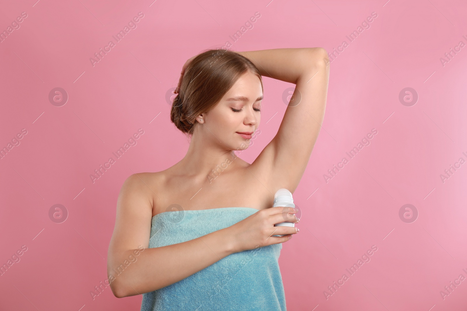 Photo of Young woman applying deodorant to armpit on pink background