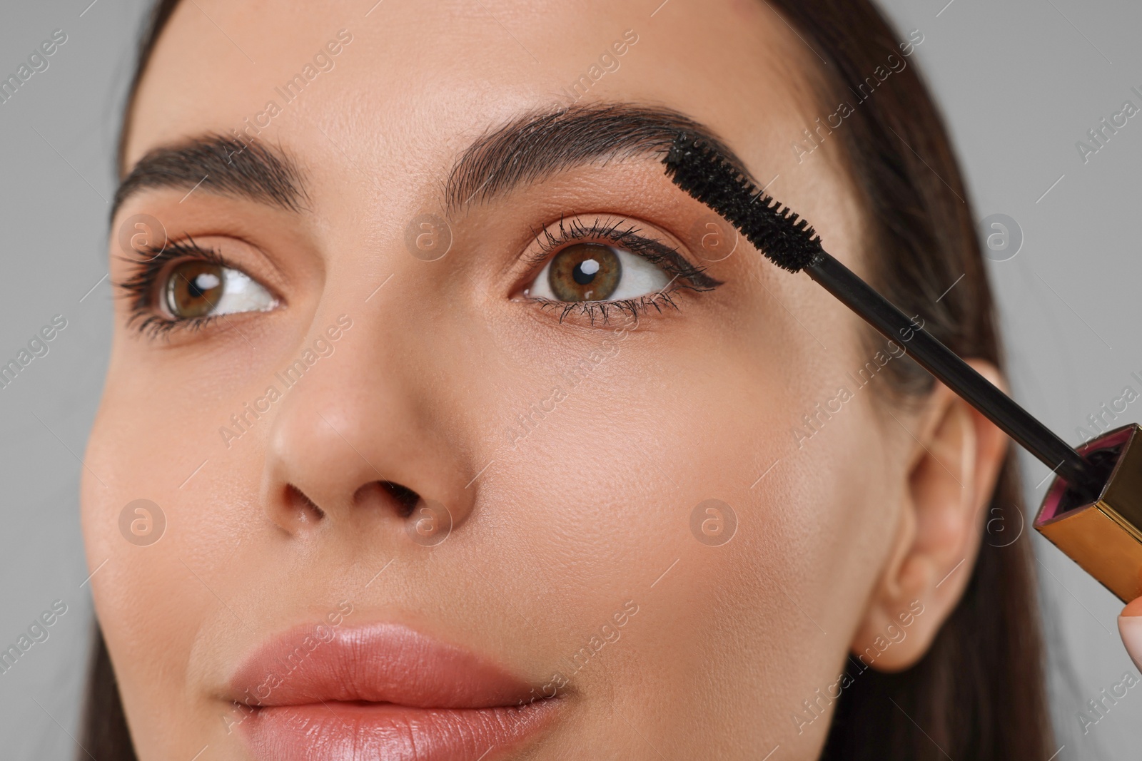 Photo of Beautiful young woman applying mascara on grey background, closeup