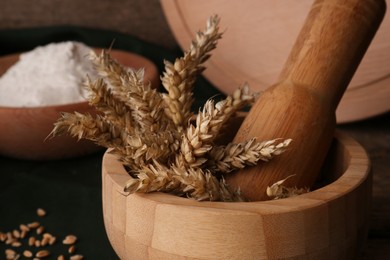 Photo of Mortar with wheat spikes on wooden table, closeup