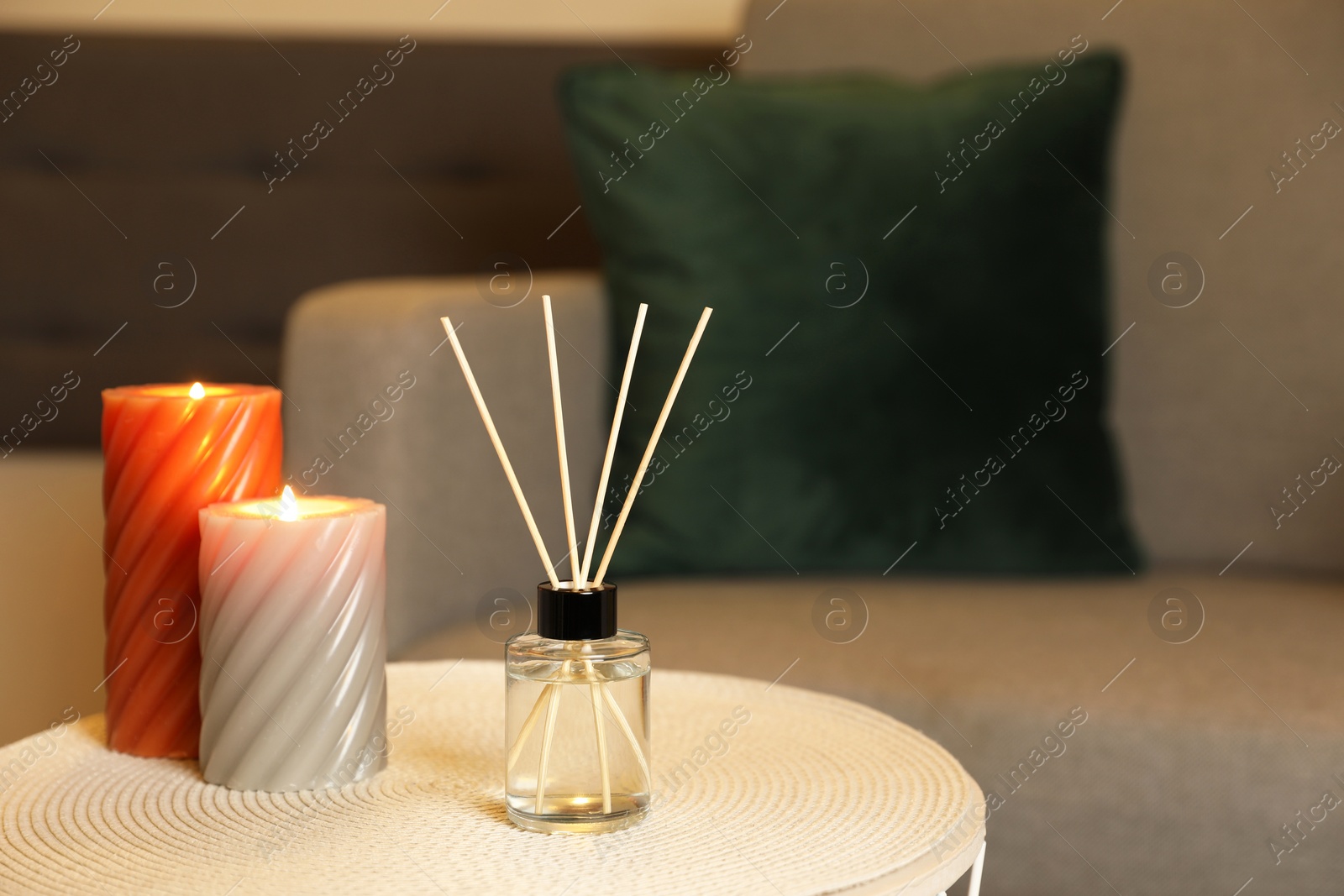 Photo of Aromatic reed air freshener and scented candles on table indoors, space for text