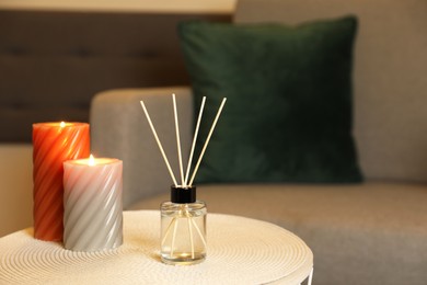 Aromatic reed air freshener and scented candles on table indoors, space for text