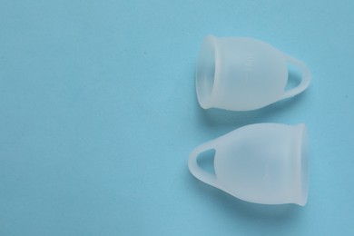 Photo of Menstrual cups on light blue background flat lay with space for text. Reusable female hygiene product