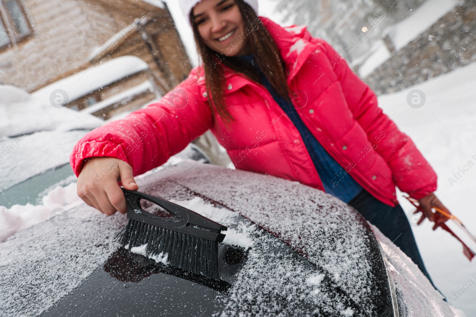 Photo of Young woman cleaning snow from car hood outdoors on winter day