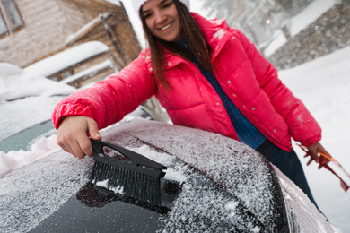 Young woman cleaning snow from car hood outdoors on winter day