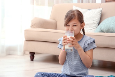 Photo of Cute little girl drinking milk on floor at home