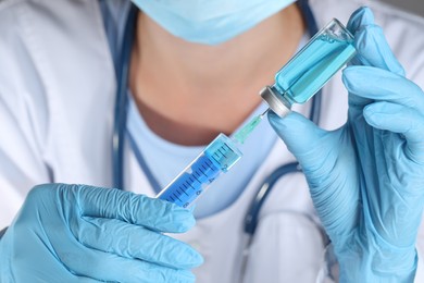 Photo of Doctor filling syringe with medication from glass vial, closeup