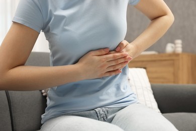 Woman suffering from stomach pain on sofa indoors, closeup