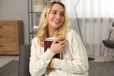 Happy woman in stylish warm sweater holding book at home