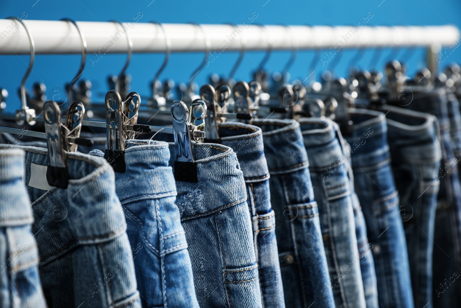 Photo of Rack with stylish jeans on blue background, closeup