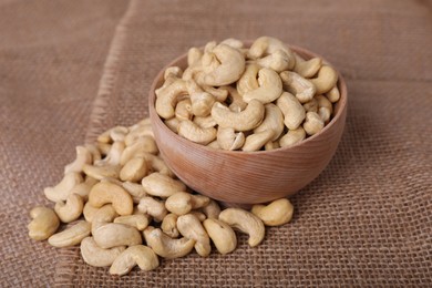 Photo of Tasty cashew nuts in bowl on light brown fabric, closeup