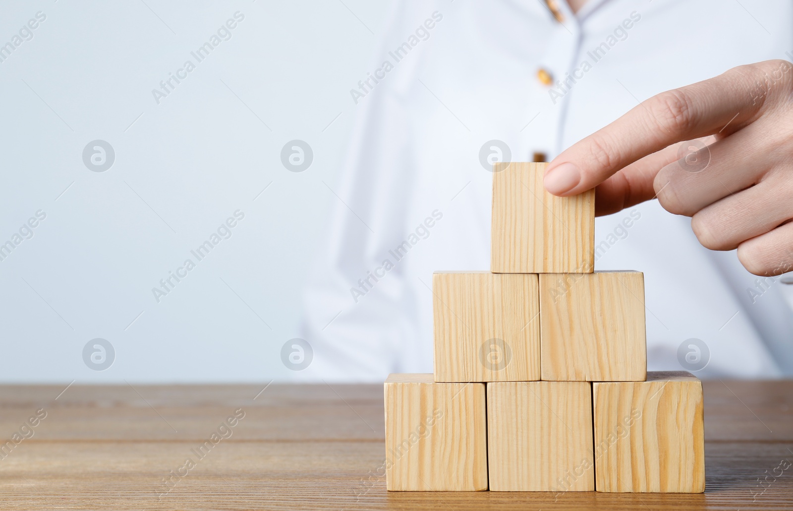 Photo of Woman building pyramid of cubes on wooden table against light background, closeup. Space for text