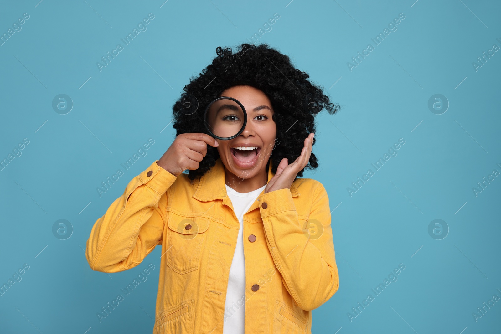 Photo of Emotional woman looking through magnifier glass on light blue background