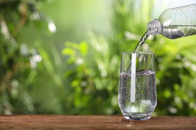 Pouring water from bottle into glass on wooden table outdoors, closeup. Space for text