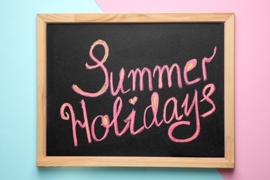 Photo of Chalkboard with phrase SUMMER HOLIDAYS on color background, top view. School's out