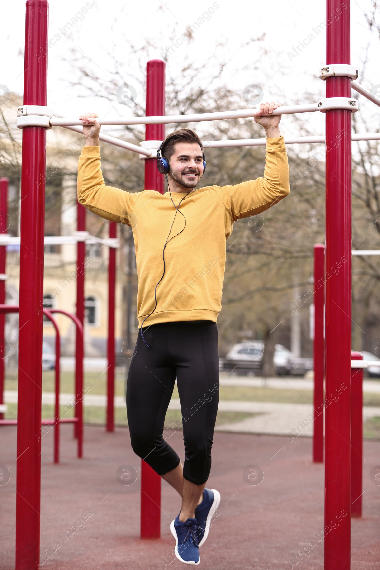 Photo of Young man with headphones listening to music and exercising on sports ground