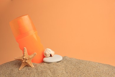 Photo of Sand with bottle of sunscreen, starfish, stone and seashell against orange background, space for text. Sun protection